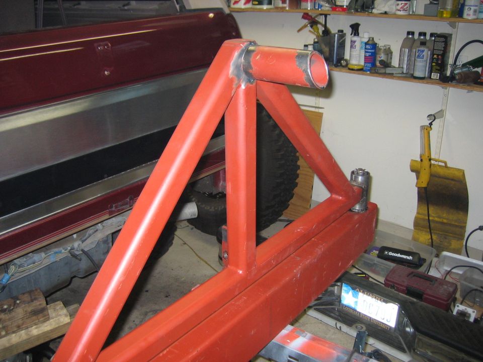 Custom red metal rear bumper and tire carrier assembly, partially attached to a vehicle. Visible tire and part of vehicle body