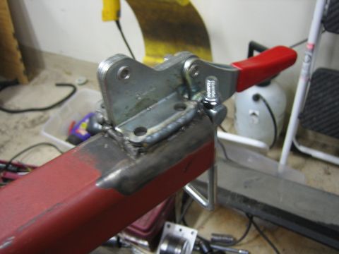 1996 Ford Bronco - A close-up view of a metal clamp assembly that has been welded onto a red beam, with various tools and equipment in the background.