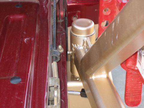 1996 Ford Bronco - Close-up of a gold metal bumper assembly with visible welds and a silver cap, attached to the red body of a vehicle.