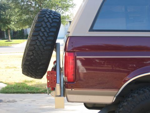 1996 Ford Bronco - The rear of a maroon and tan Ford Bronco is shown with a spare tire mounted on a swing-away carrier.