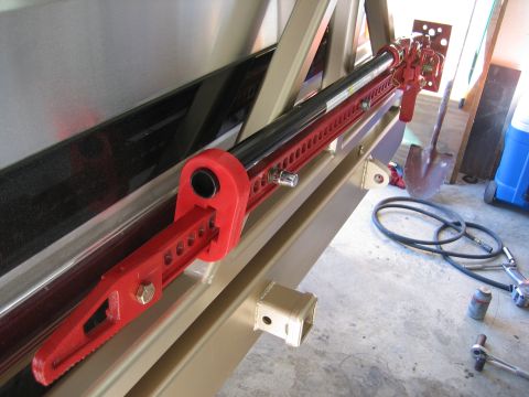 1996 Ford Bronco - A red hi-lift jack is mounted to the side of a vehicle frame, near a hitch receiver. Tools and a shovel are visible in the background.
