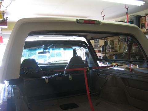 1996 Ford Bronco - Looking rearward from the cargo area of a Ford Bronco while the tan fiberglass hardtop is suspended overhead by red ratchet straps, its thi…