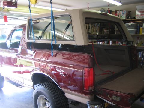 1996 Ford Bronco - dark red full-size SUV body with the white hardtop suspended above it on straps inside a home garage.