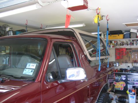 1996 Ford Bronco - A dark red full-size Ford Bronco parked in a home garage with its tan removable hardtop lifted off and suspended above the body on blue rat…