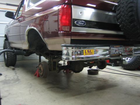 1996 Ford Bronco - The rear suspension of a 1996 Ford Bronco is visible as it is lifted for maintenance, showing the spare tire mounted on the back.