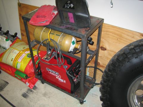1996 Ford Bronco - A welding cart holds a red Lincoln Electric welder, a yellow gas cylinder, a welding helmet, and red gloves.