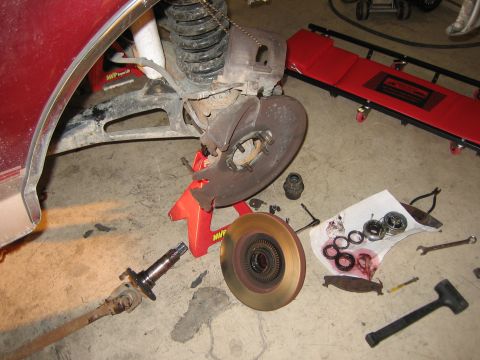 1996 Ford Bronco - Disassembled brake rotor and axle of a red vehicle, with tools and parts laid out on the floor.
