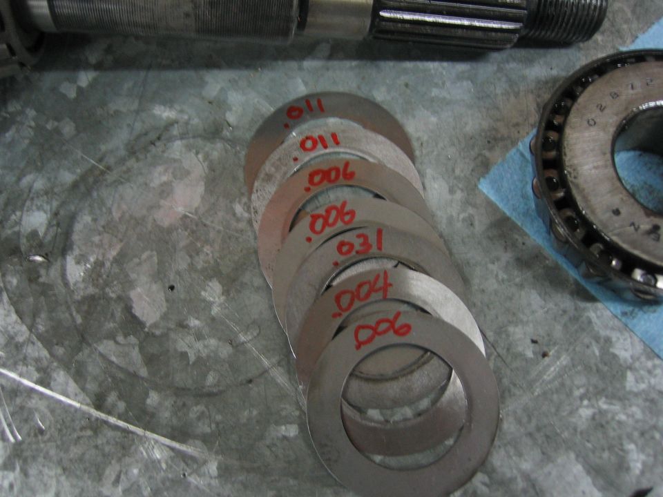 Stack of metal shims marked with thicknesses like .011, .006, .004, and .031 next to a bearing