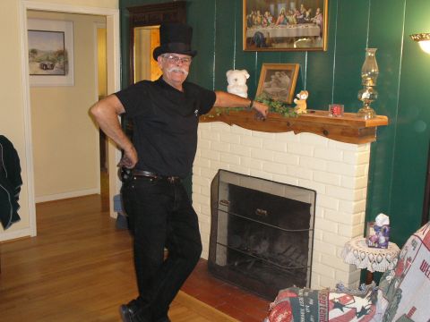 1990 Ford Bronco - A man dressed in a top hat and all black attire stands casually next to a brick fireplace adorned with decorations.