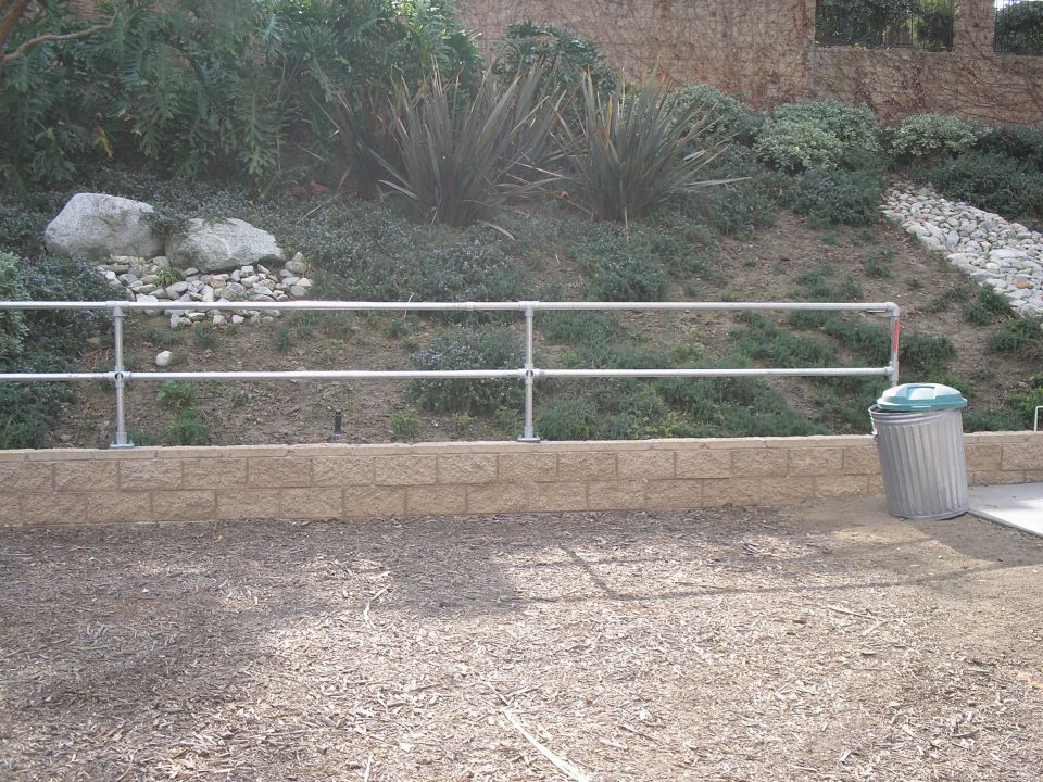 Metal pipe railing along a stone retaining wall on a landscaped hillside