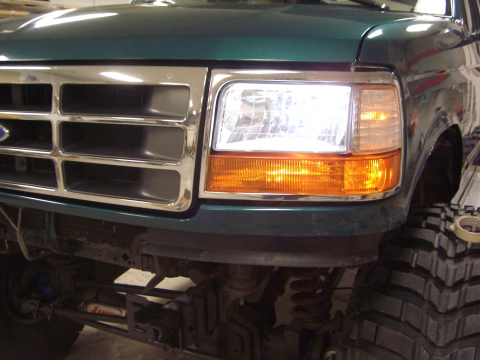 Front corner of teal Ford showing grille, headlight, and lifted suspension with large tire
