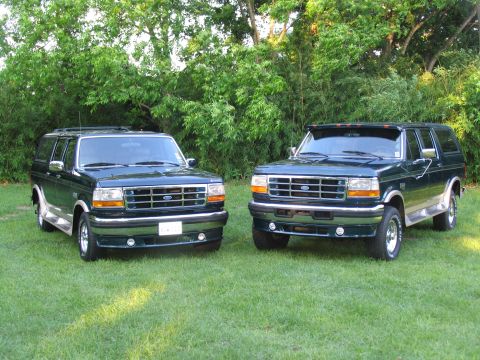 1995 Ford C-350 (Centurion Conversions) - Two Ford Bronco SUVs are parked side-by-side on a grassy lawn with trees in the background.