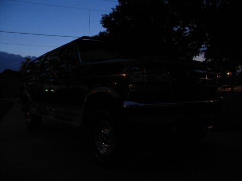 1995 Ford C-350 (Centurion Conversions) - A dark Ford F-Series truck is parked outside at twilight, with trees and a street light in the background.