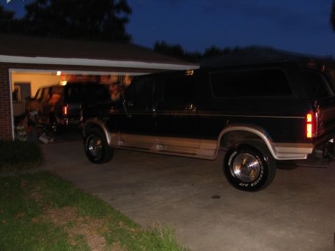1995 Ford C-350 (Centurion Conversions) - A black Ford Bronco with tan trim is parked in a driveway, with another vehicle partially visible in the garage.