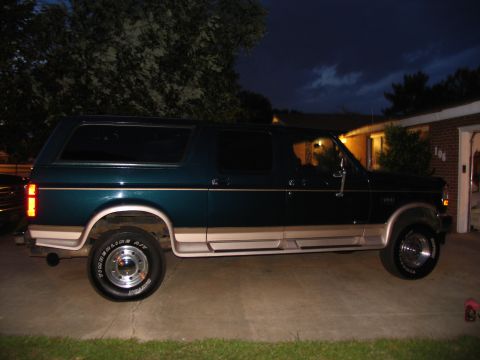 1995 Ford C-350 (Centurion Conversions) - A dark green Ford Bronco with tan trim is parked in a driveway at dusk, with a house and garage in the background.