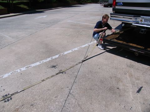 1995 Ford C-350 (Centurion Conversions) - A man secures a strap to the hitch of a Ford F-Series truck, preparing it for transport.