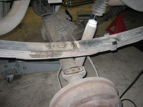 1996 Ford Bronco - Close-up view of the rear suspension system, including a leaf spring and shock absorber, with a floor jack providing support.