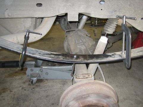 1996 Ford Bronco - Close-up view of vehicle's rear suspension components, including leaf springs and shock absorber, secured with clamps and a jack.