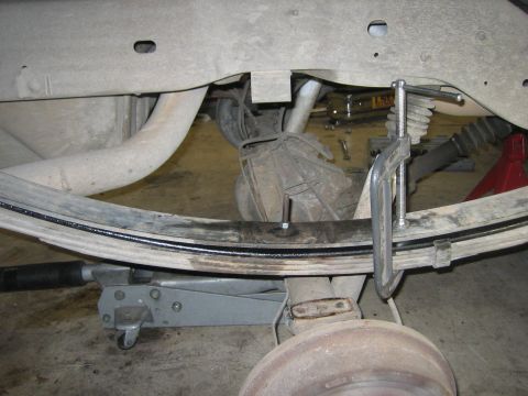 1996 Ford Bronco - Close-up of vehicle's rear suspension system, showing a leaf spring secured with a clamp and supported by a jack.