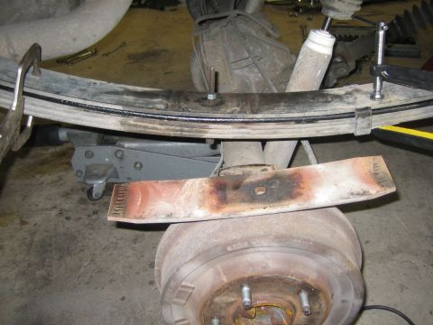 1996 Ford Bronco - Close-up view of a vehicle's rear suspension components, including a leaf spring and brake drum, with a metal blade placed on top.