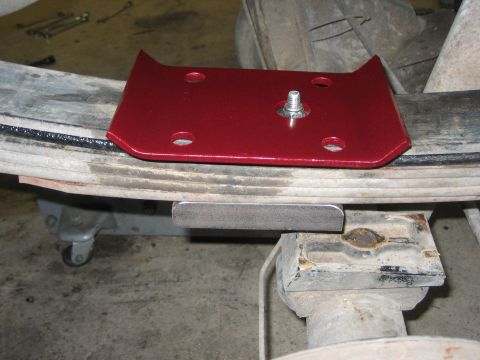 1996 Ford Bronco - A red leaf spring plate is installed on a vehicle's leaf spring, with a metal shim positioned below.