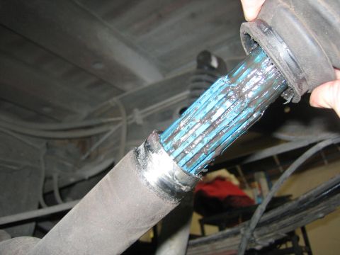 1996 Ford Bronco - A torn CV axle boot reveals the splined shaft coated in blue grease, indicating potential wear or damage.