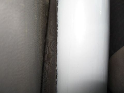 1994 Ford Bronco - Extreme close-up of a white painted body panel meeting gray textured interior trim, with a fuzzy black window-channel or weatherstrip felt…