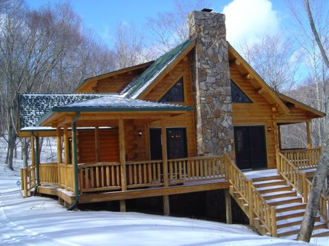 1986 Ford Bronco - A wooden log cabin sits covered in snow with a large stone chimney and a covered porch.