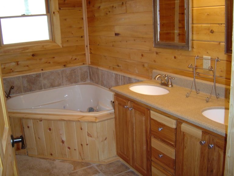 Bathroom with a corner tub, double vanity, and wood paneling. Supermotors.net logo in corner