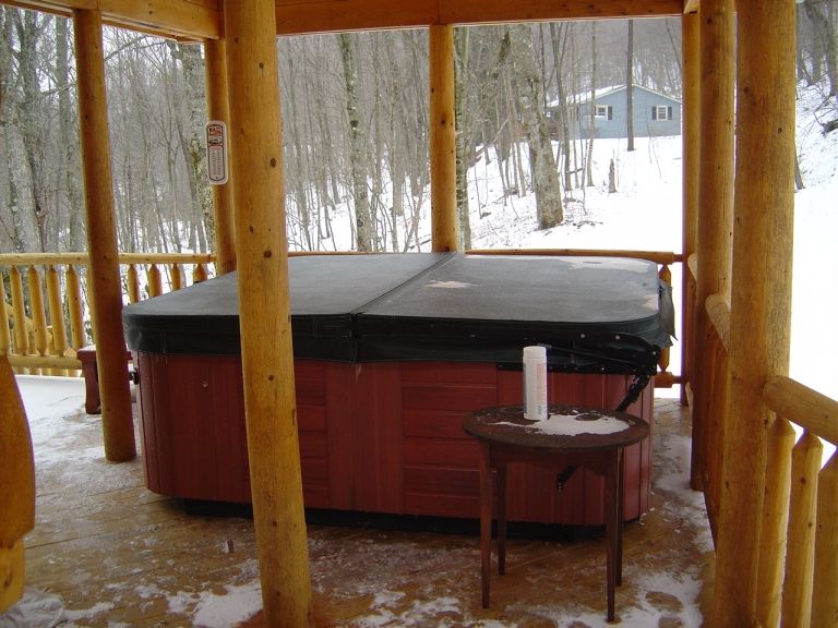 Hot tub on a wooden deck with snow on the ground and trees in the background