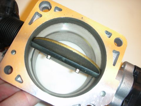 1998 Ford Crown Victoria - Close-up of a throttle body with the butterfly plate open inside the bore, held by hand over a white surface.