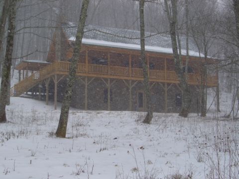 1986 Ford Bronco - A rustic cabin is seen through falling snow, with trees and a snowy landscape.