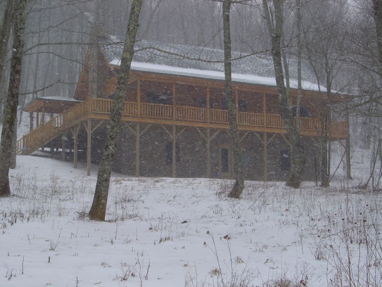 Wooden cabin with a large porch surrounded by trees during a snowstorm