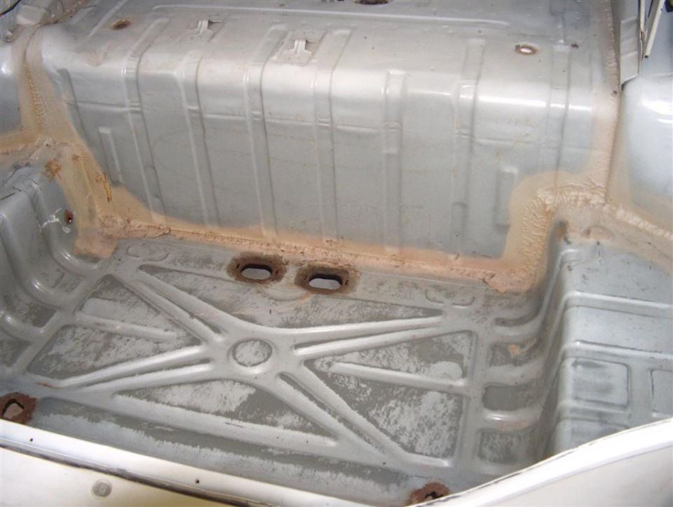 Underside of a car floor pan showing fuel tank and central X-brace