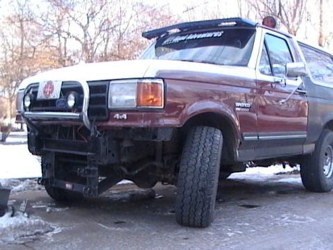 1990 Ford Bronco - A maroon and white Ford Bronco with a custom bumper and a "Allied Adventures" banner on the windshield sits in a snowy area.