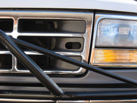 1994 Ford Bronco - Close-up of the front end of a Ford Bronco/F-series truck showing the chrome-trimmed grille with rectangular slots, a right-side headlight…