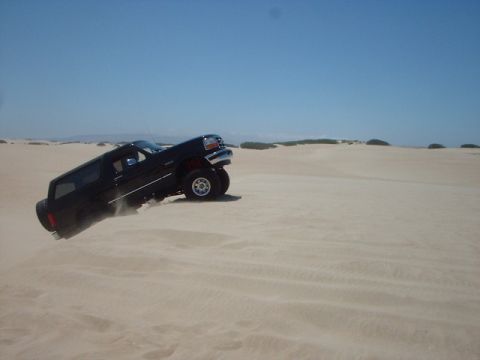 1996 Ford Bronco - A black 1996 Ford Bronco navigates sandy terrain under a clear blue sky.