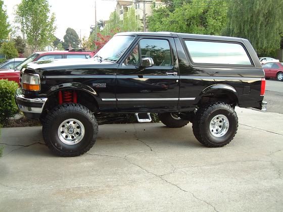 Black lifted two-door Ford Bronco SUV on large tires, side view in a driveway