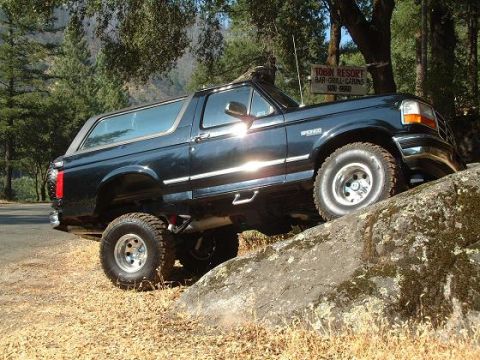 1996 Ford Bronco - A dark blue Ford Bronco is shown navigating a rocky terrain with its suspension lifted.