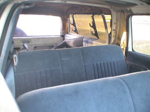 1993 Ford C-350 (Centurion Conversions) - The interior of a van shows two rows of blue velour seats and hooks mounted on the rear window frame.