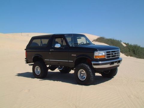 1996 Ford Bronco - This black 1996 Ford Bronco is shown off-road in a sandy environment with dunes and sparse vegetation.