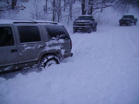 2000 Chevrolet Tahoe - Multiple vehicles navigate a snow-covered road, with one SUV deeply stuck in the snow.