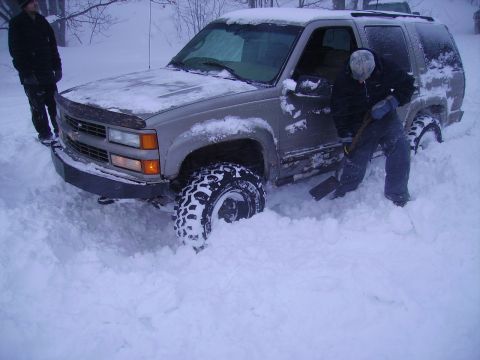 2000 Chevrolet Tahoe - A person digs out a stuck SUV from deep snowdrifts, with another person watching.