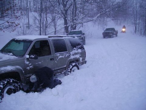 2000 Chevrolet Tahoe - Several vehicles are stuck in the snow, with one person attempting to free an SUV.