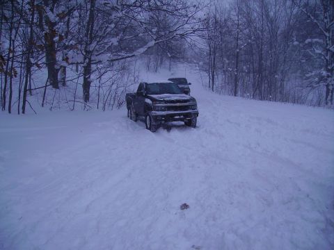2000 Chevrolet Tahoe - A dark pickup truck is stuck in the snow, with another vehicle visible behind it in the distance.