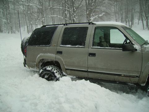 2000 Chevrolet Tahoe - SUV stuck in snowdrift with trees in background.