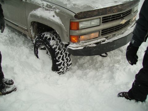 2000 Chevrolet Tahoe - This truck is stuck in the snow. The front tire is completely buried. People are standing around it.