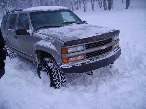 2000 Chevrolet Tahoe - A silver Chevrolet Tahoe with aggressive tires is stuck in deep snow, with trees in the background.