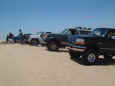 1996 Ford Bronco - Several SUVs and trucks are parked on a sandy beach under a clear blue sky.