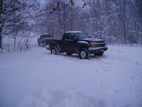 2000 Chevrolet Tahoe - Two pickup trucks navigate a snow-covered road in a wooded area.